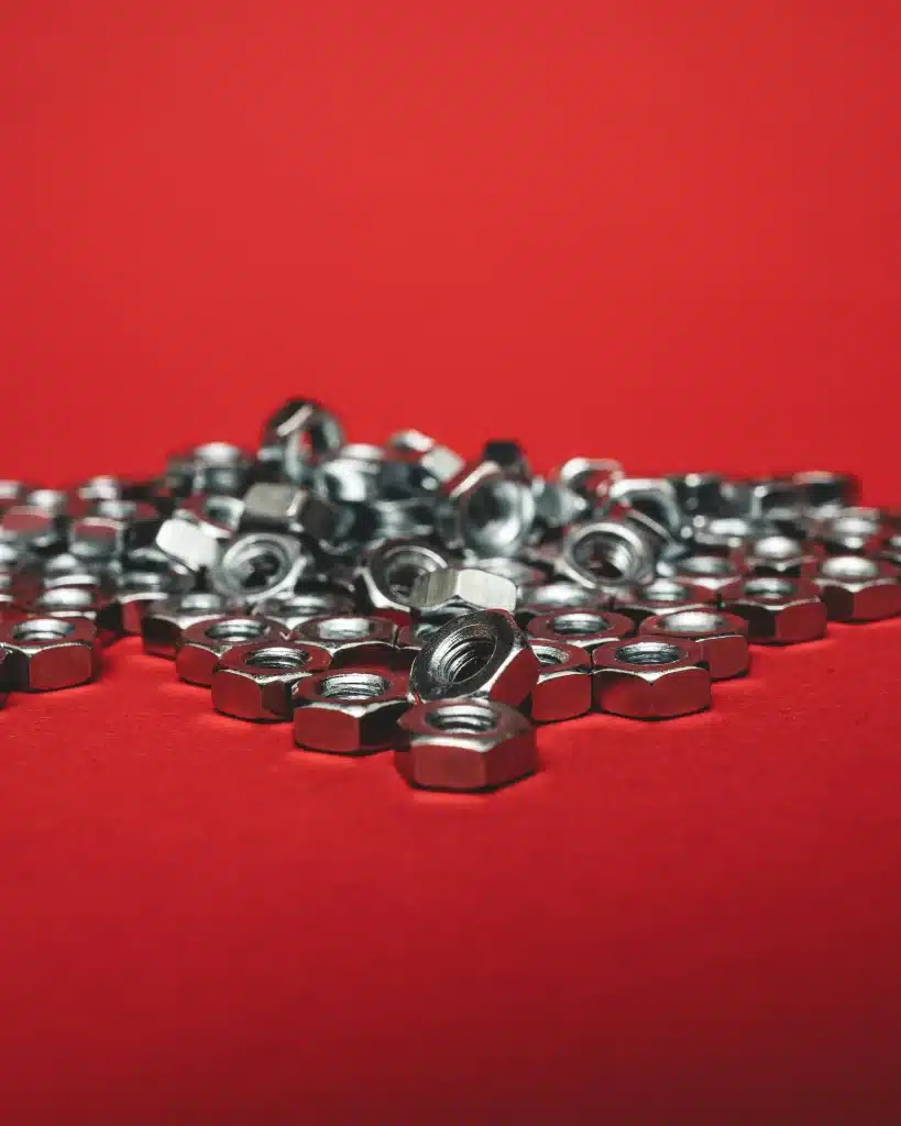 A close-up image of shiny metal bolts arranged in a row on a red background.